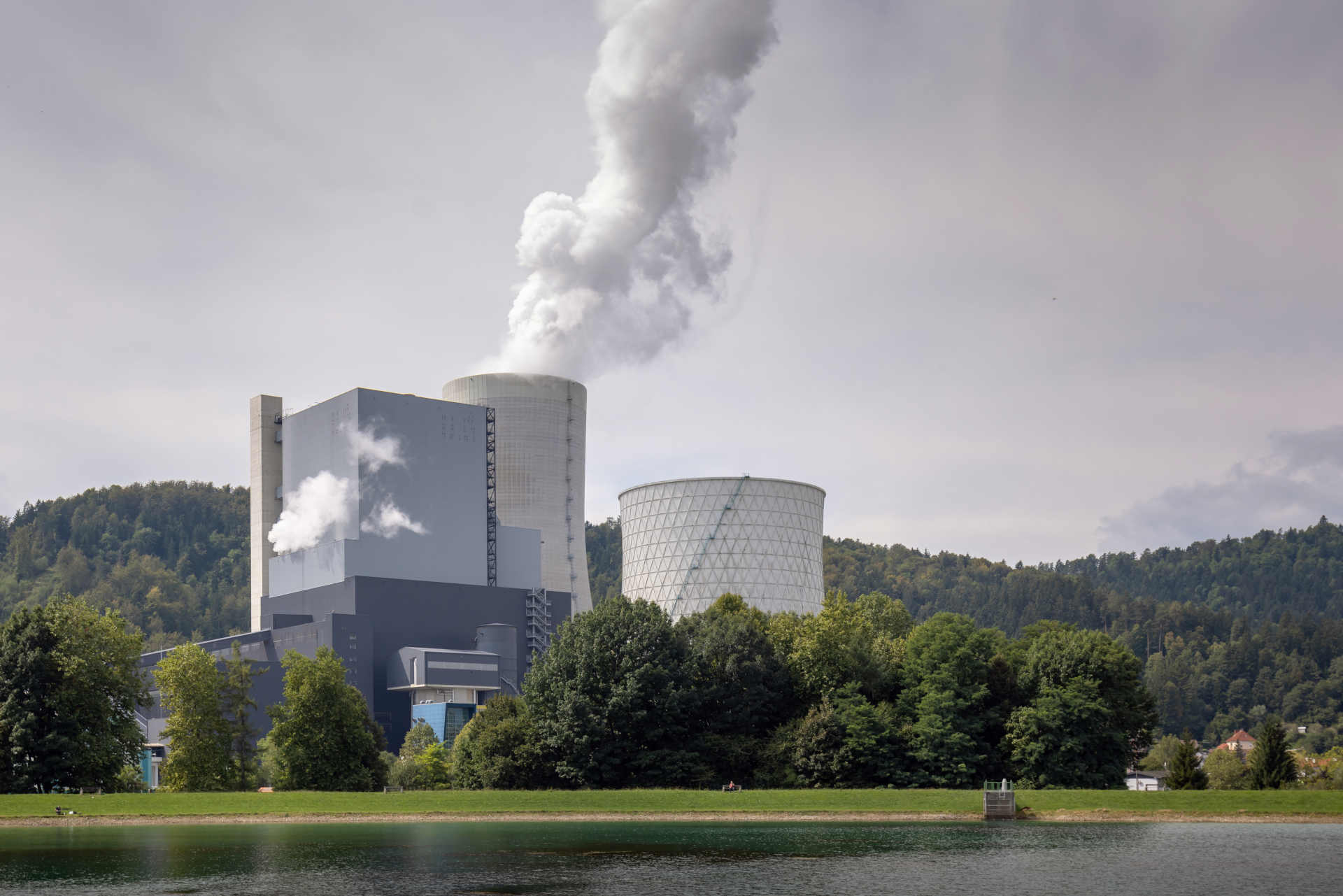 Smoking chimney at thermal power plant near lake and green nature.